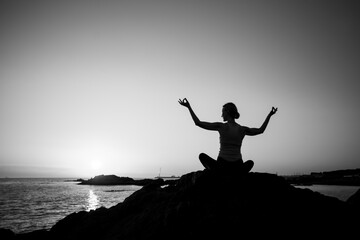 Yoga silhouette of a woman in lotus pose on the ocean during sunset. Black and white photo. - 598032529