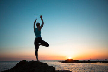 Fototapeta premium A silhouette of a yoga woman on the ocean shore during sunset.