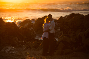 A young couple in love on the oceanfront during a golden sunset.