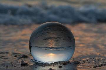 Crystal ball with reflection on sea beach and sunset light background. Beautiful seascape on evening time. Summer travel and vacation concept.