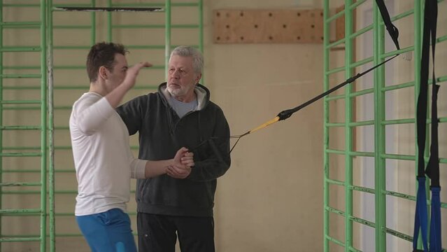 young caucasian man is engaged in strength fitness using TRX loops in the gym, a personal trainer is watching an athletic young man, active training. High quality Full HD video recording Generative AI