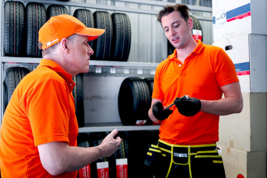 Two auto mechanic men talking during checking wheel tires at vehicle repair service shop, senior and young men working in garage, car service technician checking warehouse stock at automobile car shop