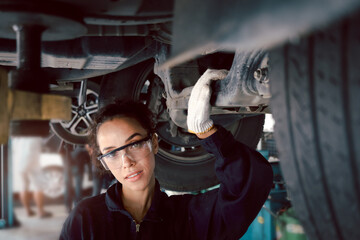 Beautiful female auto mechanic checking wheel tires in garage, car service technician woman repairing customer car at automobile service, inspecting vehicle underbody and suspension engine system.