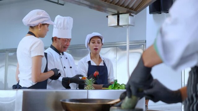 Team chef instruction and explaining apprentice about cooking and preparing vegetable fresh for food together in the kitchen, man training and discussing assistant woman about preparing recipe meal.