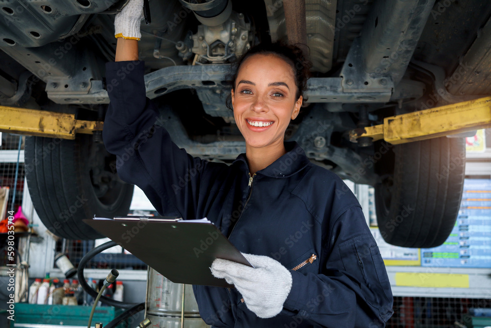 Wall mural beautiful female auto mechanic checking wheel tires in garage, car service technician woman repairin