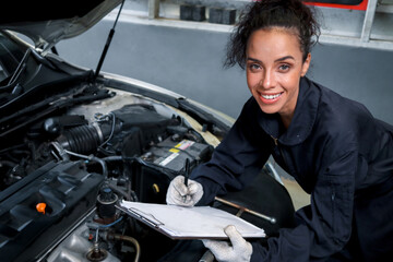 Beautiful female auto mechanic working in garage, car service technician woman holding file paper...