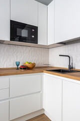 kitchen interior, white cabinet fronts, induction cooker, sink, microwave oven, white tiles on the...