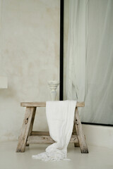 Rustic, vintage wooden light brown stool draped with white linen throw in modern, minimal, white...