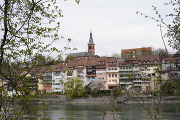 Fototapeta na wymiar Catholic Church of St. John Baptist with Rhine river on the foreground. The church is surrounded by historical buildings and trees with some leaves in springtime.