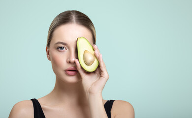 Portrait of a young woman with clear skin holding half an avocado to her face.