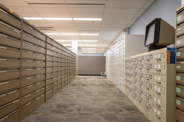 Rows of beige and brown filing cabinets in an empty office with fluorescent lighting and brown carpet tiles,  microfilm reader, nobody	