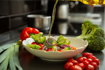Cooking fresh vegetables salad in the kitchen at home. Healthy eating and lifestyle concept. Adding extra virgin olive oil from the bottle. 
