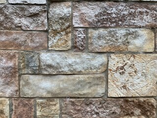 Stone wall closeup, grunge texture for background. Old building facade, hewn granite blocks of dissimilar shape and color with rough weathered surface. Geometric pattern of exterior masonry.