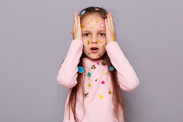 Shocked scared little girl covered colorful kid's stickers standing isolated over gray background...