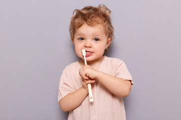 Funny little child baby brushing teeth isolated over gray background oral care using kid's...