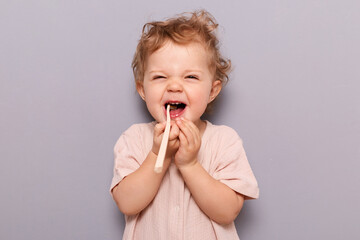 Oral hygiene. Dental care. Laughing funny little child baby brushing teeth isolated over gray background enjoying wearing t-shirt, free space for advertisement.