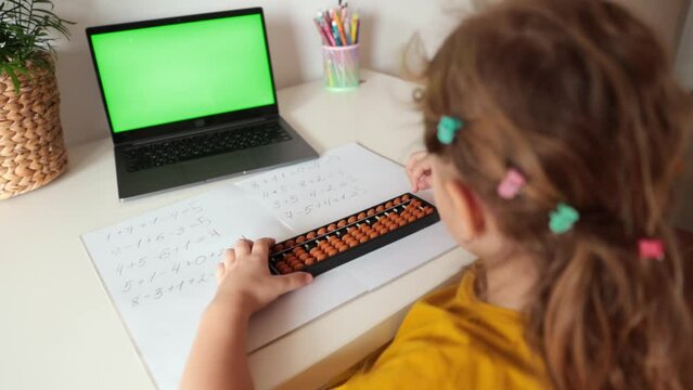 A girl from the back is engaged in mental arithmetic on the abacus online on a laptop, chroma key background. The concept of teaching children to count quickly, Russian mathematics.