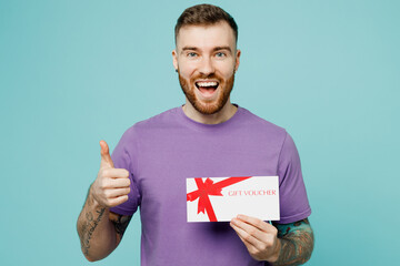 Young man wears purple t-shirt hold gift certificate coupon voucher card for store show thumb up...