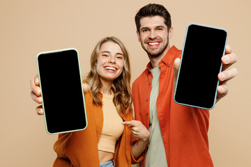 Young smiling couple two friend family man woman wear casual clothes hold in hand use showing close up mobile cell phone with blank screen workspace area together isolated on plain beige background. - Powered by Adobe