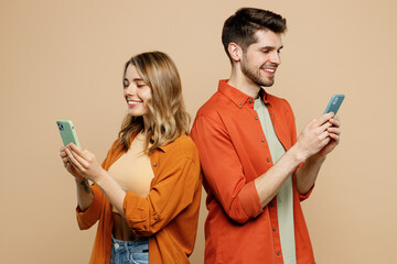 Side view young couple two friends family man woman wear casual clothes hold in hand use mobile cell phone together stand back to back isolated on pastel plain light beige background studio portrait.