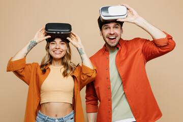 Young amazed fun couple two friends family man woman wear casual clothes looking camera together taking off vr headset pc gadget isolated on pastel plain light beige color background studio portrait.