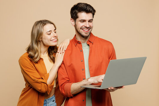 Sideways young happy couple two friends family IT man woman wearing casual clothes hold use work on laptop pc computer together isolated on pastel plain light beige color background studio portrait.
