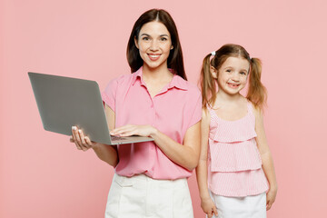 Happy smiling IT woman wear casual clothes with child kid girl 6-7 years old. Mother daughter hold use work on laptop pc computer isolated on plain pastel pink background. Family parent day concept.