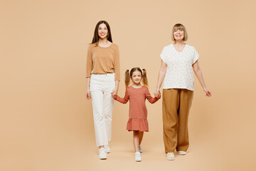 Full body smiling fun cheerful women wearing casual clothes with child kid girl 6-7 years old. Granny mother daughter walk holding hands isolated on plain beige background. Family parent day concept.