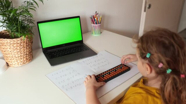 A girl from the back is engaged in mental arithmetic on the abacus online on a laptop, chroma key background. The concept of teaching children to count quickly, Russian mathematics.
