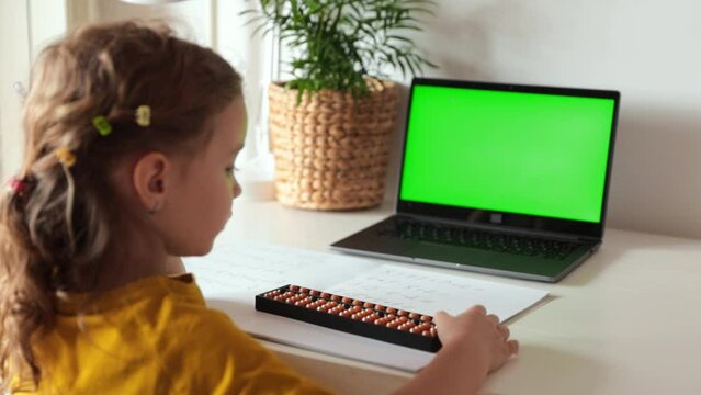 A girl from the back is engaged in mental arithmetic on the abacus online on a laptop, chroma key background. The concept of teaching children to count quickly, Russian mathematics.