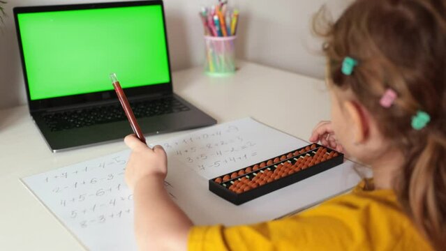 A girl from the back is engaged in mental arithmetic on the abacus online on a laptop, chroma key background. The concept of teaching children to count quickly, Russian mathematics.