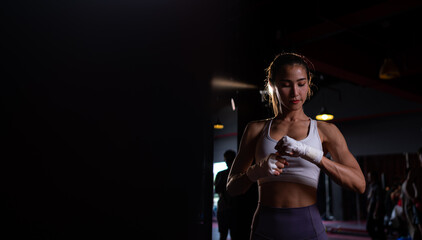 Fototapeta na wymiar Portrait of woman learning Muay Thai to build up the strength of the body and use it for self-defense. Are using hand wraps before putting on boxing gloves for boxing