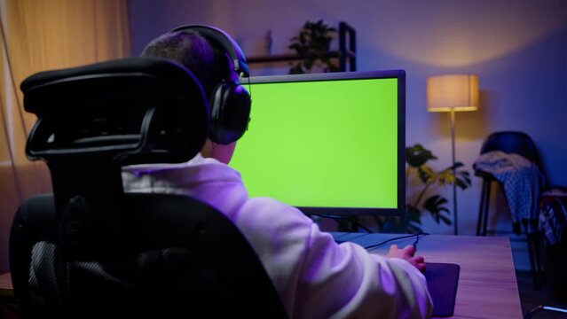 Young gamer in hoodie plays game on computer with chromakey