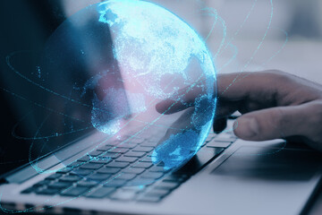 Close up of businessman hand using laptop keyboard at desktop with glowing blue polygonal globe on blurry background. Global technology and metaverse concept. Double exposure.