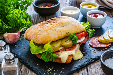 Ciabatta  sandwich with salami, mozzarella, lettuce, tomato, cucumber and dressing on wooden table
