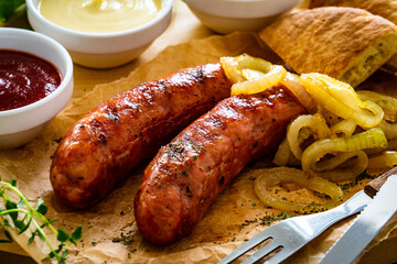 Fried sausages, onion and bread on wooden table
 - obrazy, fototapety, plakaty