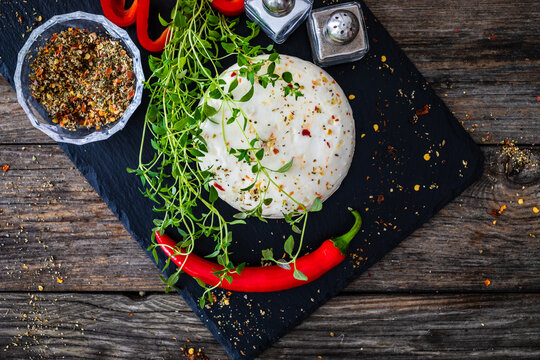 Cheese Robiola d'Alba with chili and thyme on black stone board on wooden table