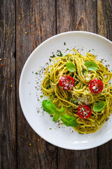 Noodles with basil pesto, parmesan cheese, tomatoes and basil leaves served on wooden table 