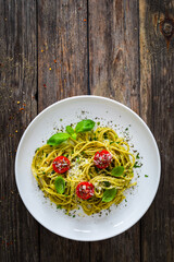 Noodles with basil pesto, parmesan cheese, tomatoes and basil leaves served on wooden table 