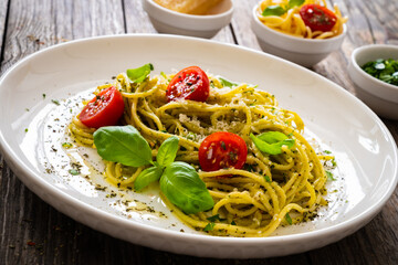 Noodles with basil pesto, parmesan cheese, tomatoes and basil leaves served on wooden table 