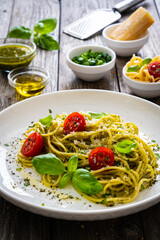 Noodles with basil pesto, parmesan cheese, tomatoes and basil leaves served on wooden table 