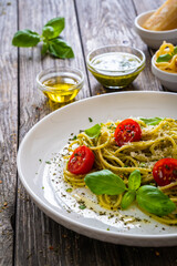 Noodles with basil pesto, parmesan cheese, tomatoes and basil leaves served on wooden table 