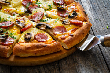 Circle pizza with sausages, onion and mozzarella cheese on wooden table 