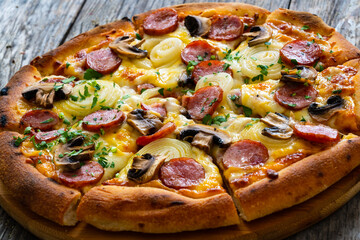 Circle pizza with sausages, onion and mozzarella cheese on wooden table 
