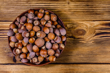 Plate with pile of hazelnuts on a wooden table. Top view