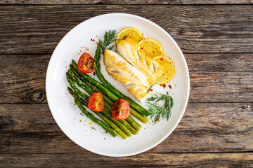Fried halibut loin with cooked green asparagus and tomatoes on wooden table
 - obrazy, fototapety, plakaty