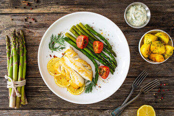 Fried halibut loin with cooked green asparagus and tomatoes on wooden table
