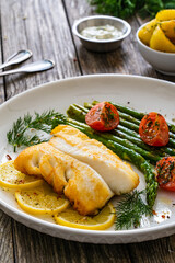 Fried halibut loin with cooked green asparagus and tomatoes on wooden table
