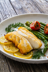 Fried halibut loin with cooked green asparagus and tomatoes on wooden table
