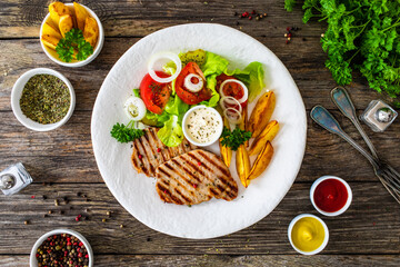Barbecued pork chops with fried potatoes and fresh vegetables on wooden table
